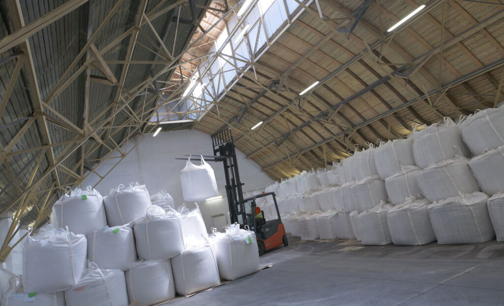 Many stacked one tonne bags of sugar in a warehouse with a forklift