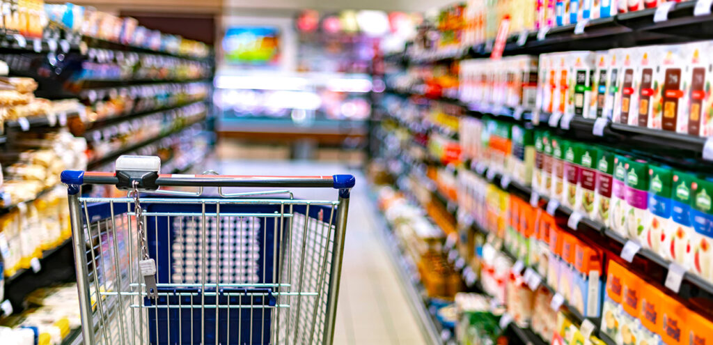 A trolley sits off centre in the left side of a well stocked supermarket isle filled with colourful products