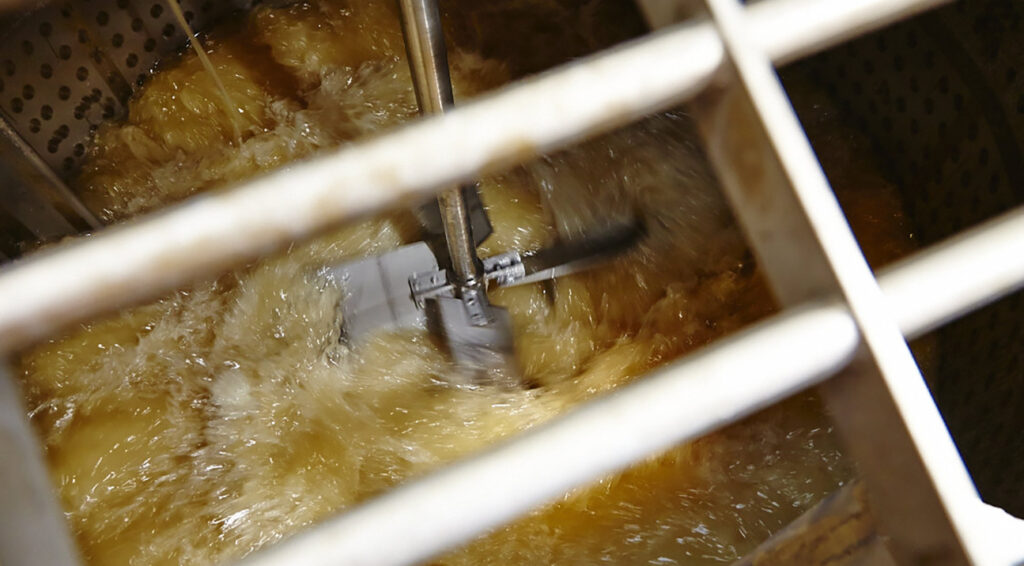 An industrial mixer is photographer churning a yellow coloured liquid in a metal vat