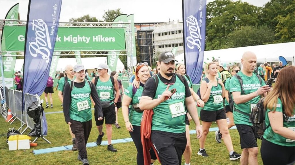 A group of people wearing green shirts and bibs begin their charity walk leaving the starting line