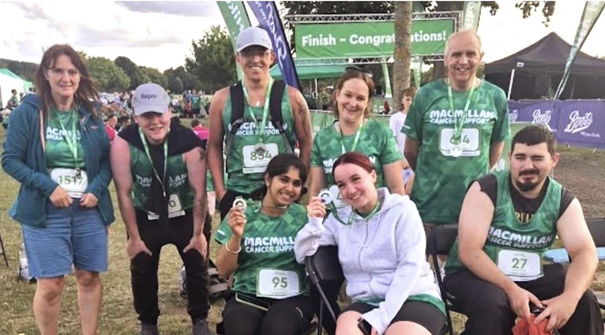 A group of 8 people wearing green shirts smiling at the finish line while holding medals