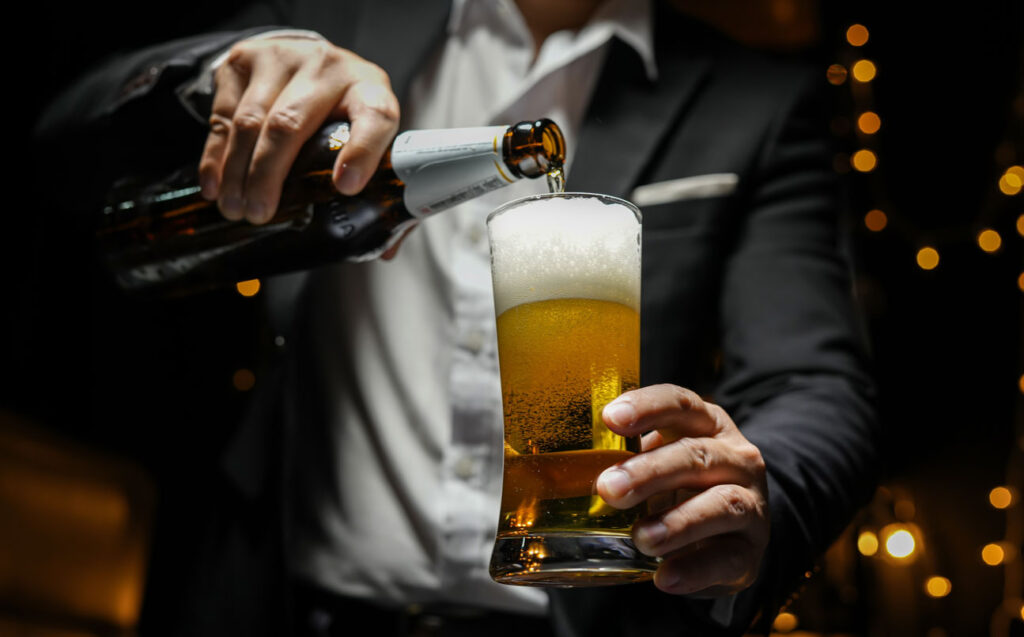 A brown bottle of beer is being poured into a pint glass